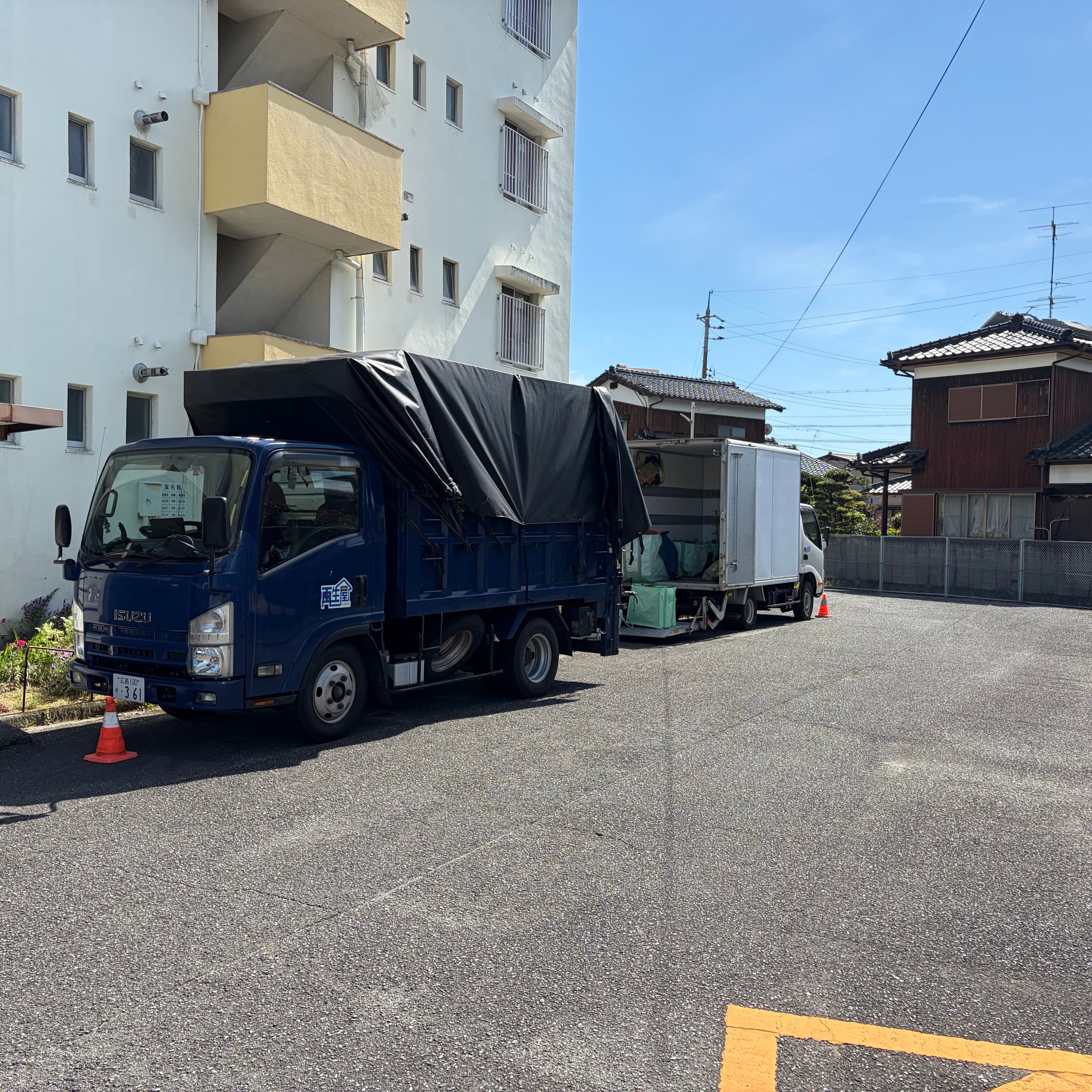 マンション前の駐車場に並んだ再生屋の作業車。青い軽トラックと白いボックストラック。